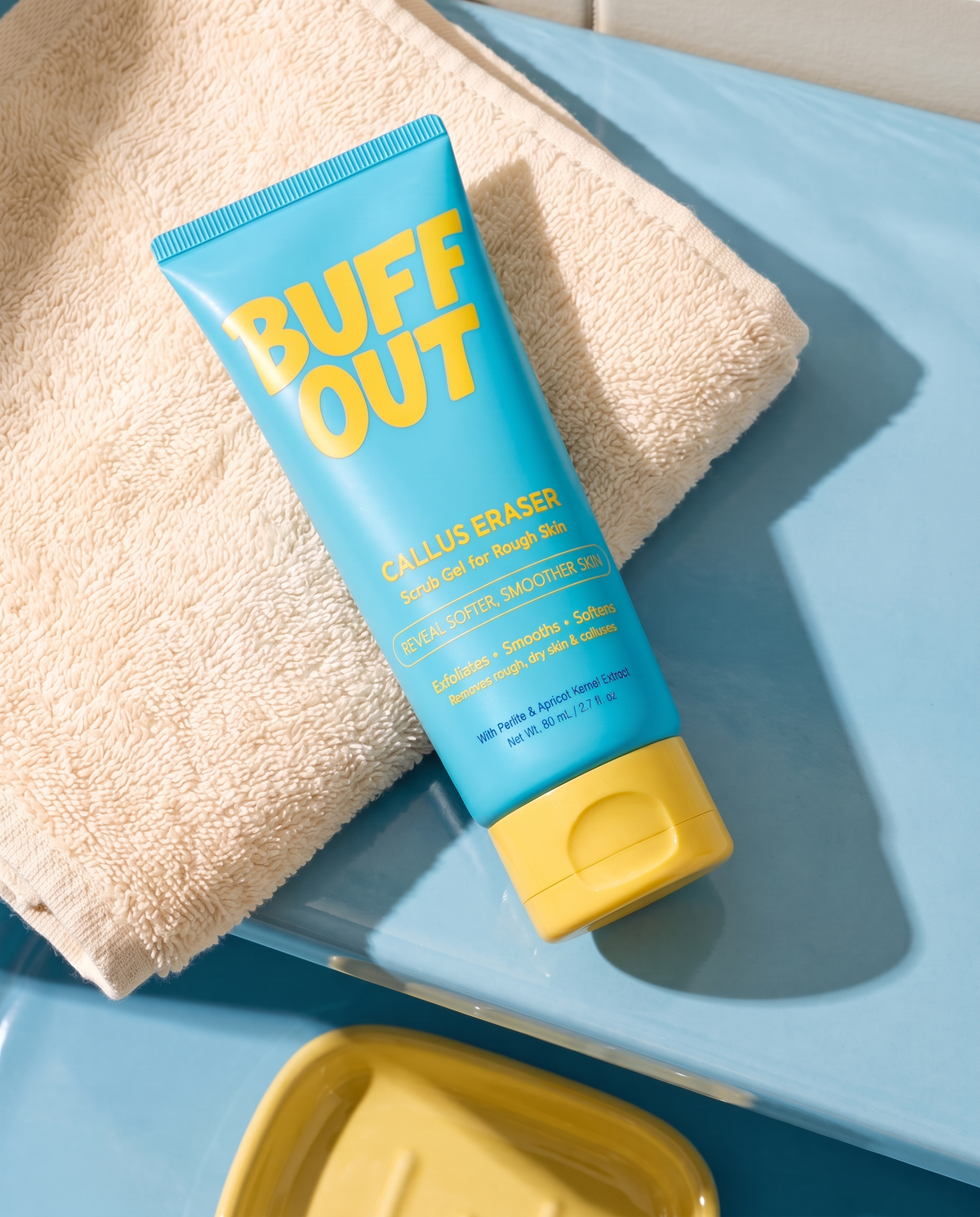 BuffOut Callus Eraser resting on a cream towel on a blue bathroom shelf